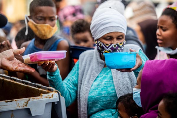Woman at a soup kitchen wearing a facemask with plates of food in each hand