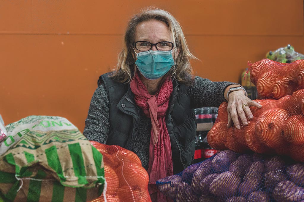 Ladles of Love staff member looks into camera wearing glasses and facemasks, behind vegetables