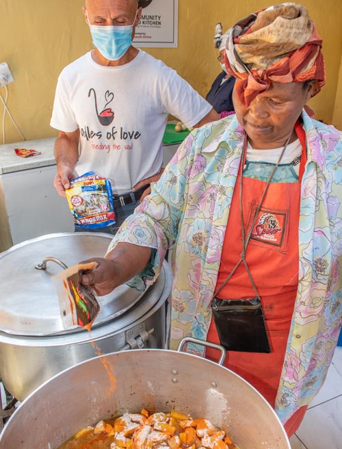 Mama Victoria seasons a pot of soup she's cooking in her community kitchen, with Ladles of Love founder Danny by her side
