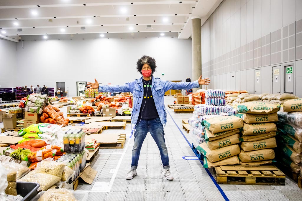 Comedian Marc Lottering stands with his arms out in the Ladles of Love warehouse, showing off the fresh produce donations