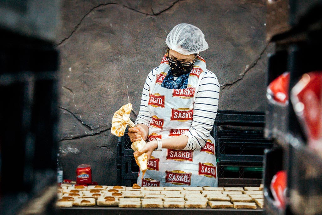 A volunteer in a SASKO apron pipes peanut butter into sandwiches as part of a Ladles of Love charity team building event